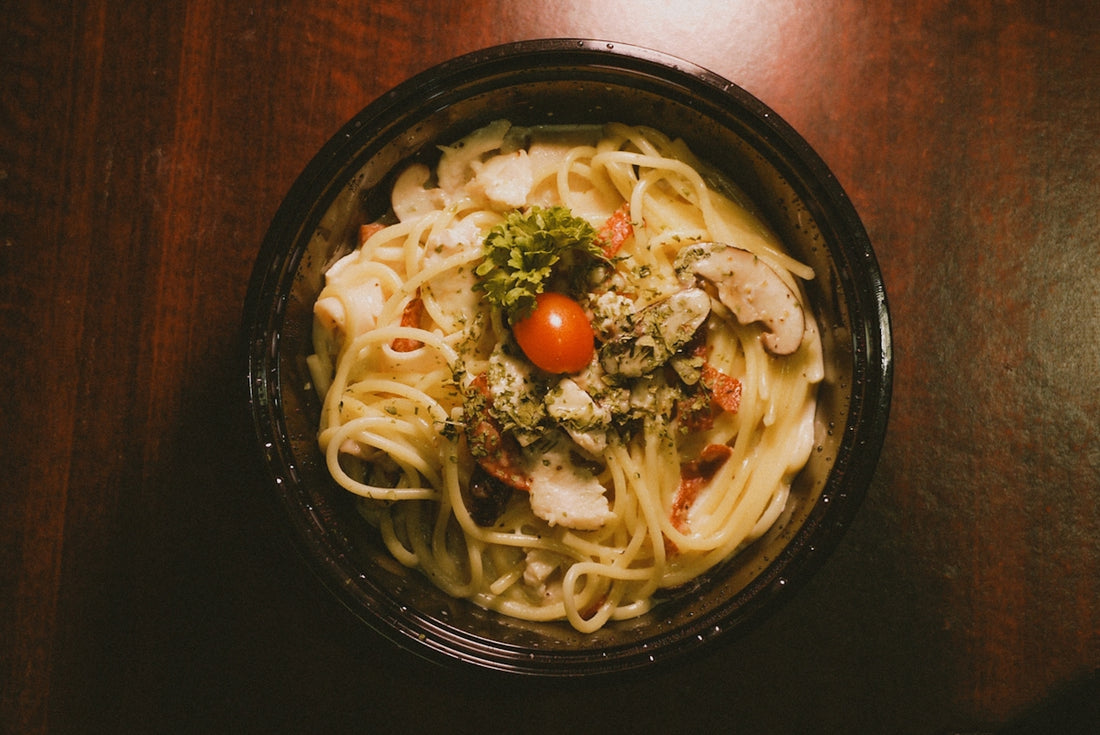 A bowl of pasta with a tomato and broccoli on top