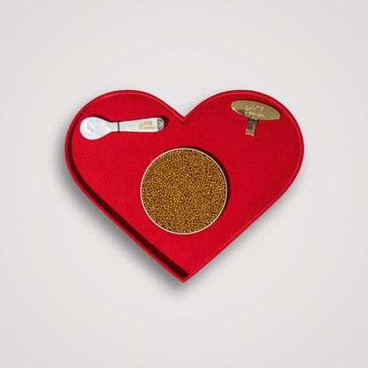 Red heart-shaped tray with a gold circular item and silver spoon on a light gray background
