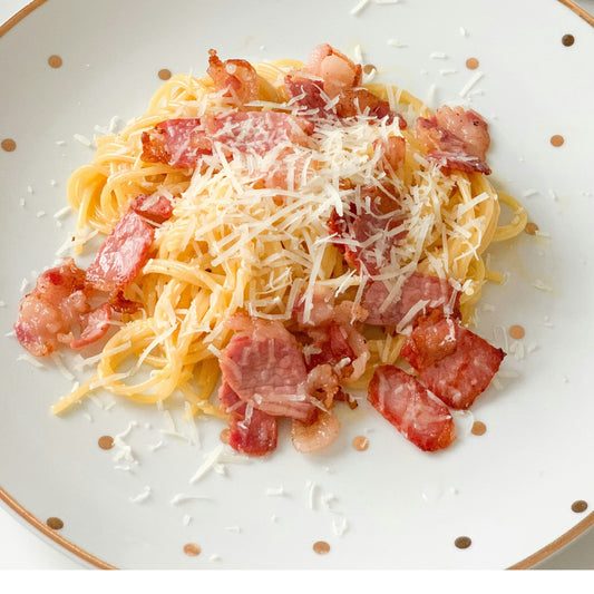 Spaghetti with bacon on a white plate with gold rim