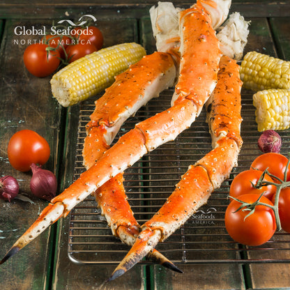 Large crab legs on a metal surface with corn, tomatoes, and onions, branded 'Global Seafoods North America'.