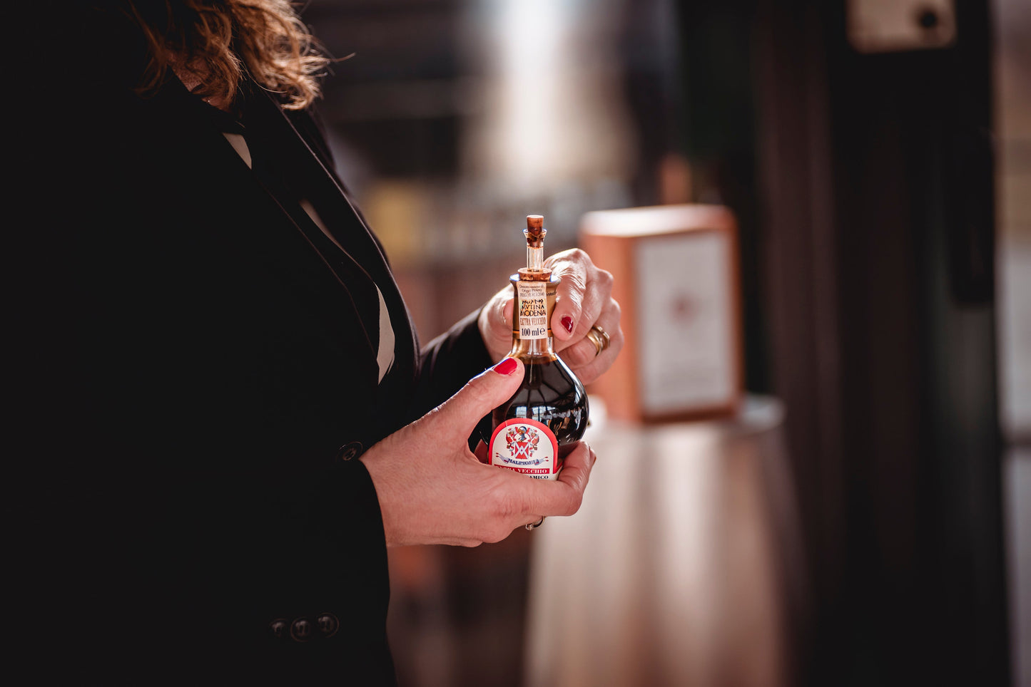 Person holding a small bottle with a red label in a blurred indoor setting