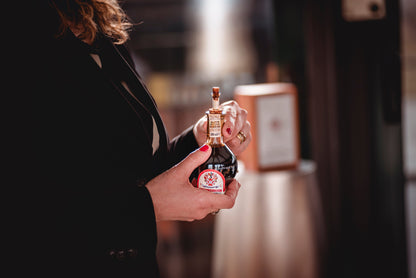 Person holding a small bottle with a red label in a blurred indoor setting