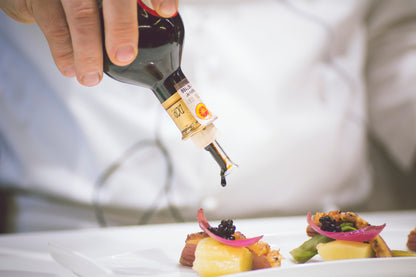 Person pouring a Balsamic over a dish of food on a white surface.