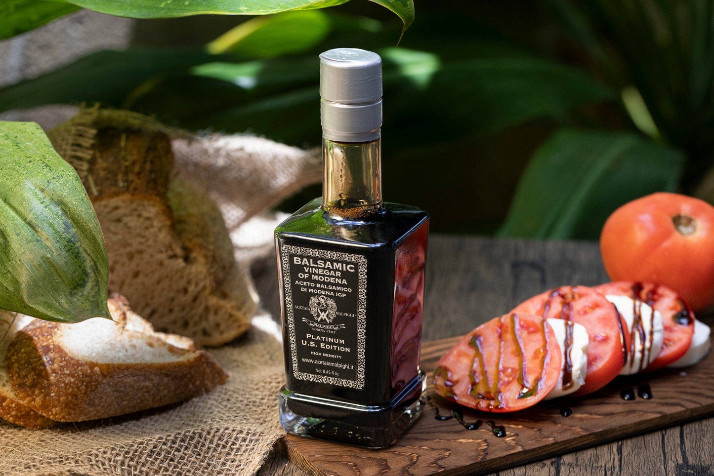 Balsamic vinegar bottle on a wooden board with bread and tomatoes