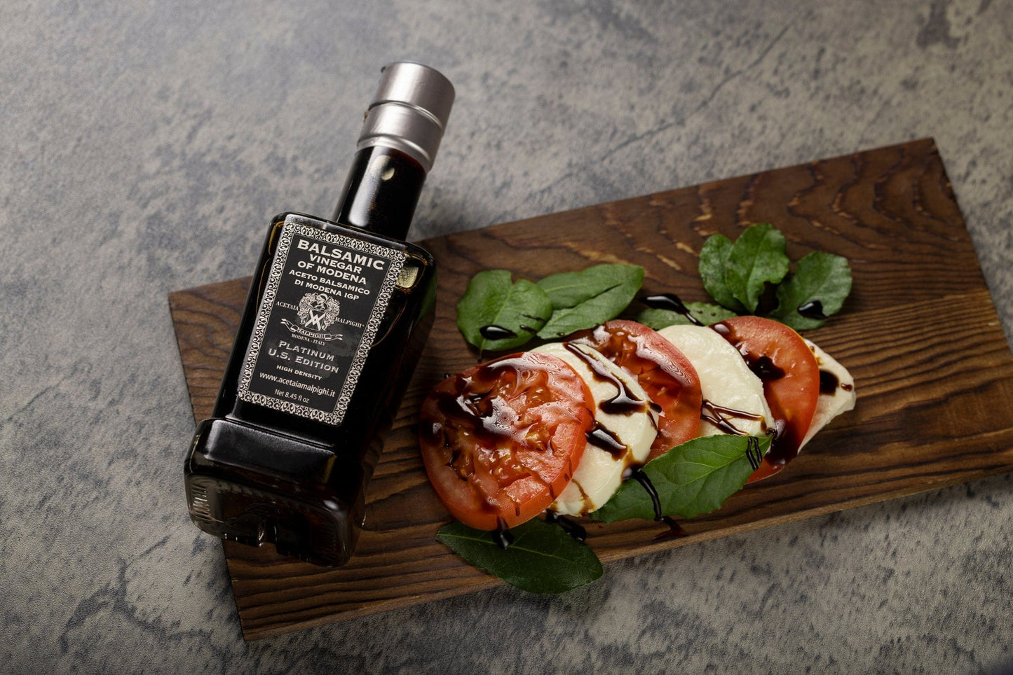 Balsamic vinegar bottle next to a caprese salad on a wooden board
