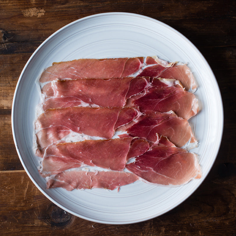 Slices of prosciutto on a white plate on a wooden surface