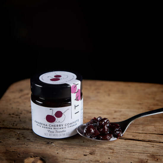 Jar of Amarena Cherry Compote with a spoonful on a wooden surface