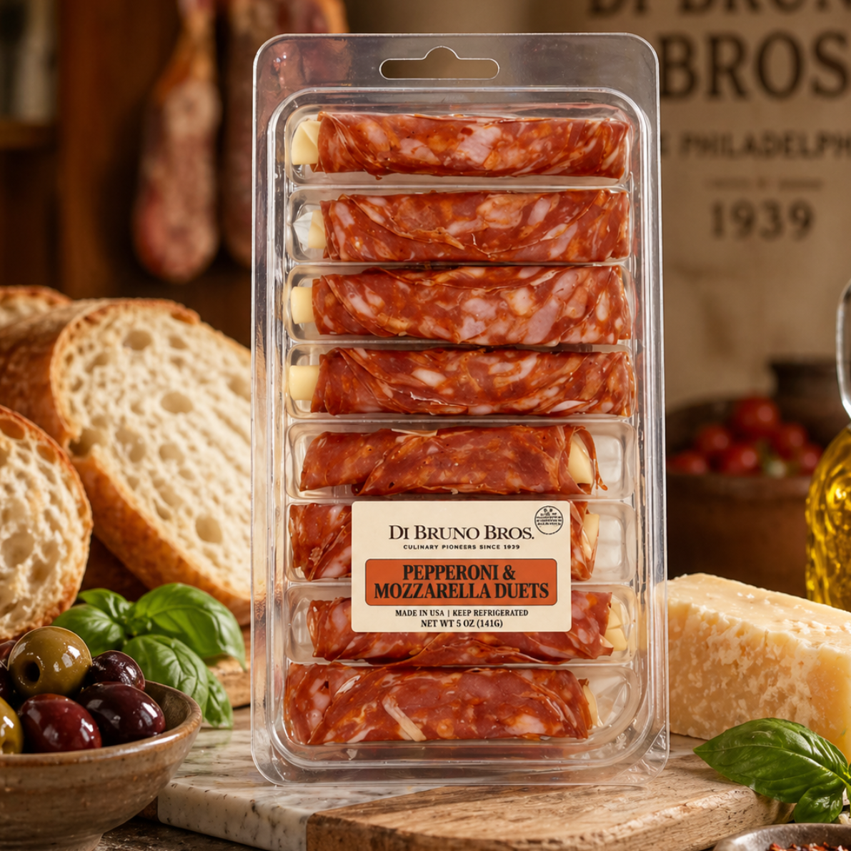 Packaged pepperoni and mozzarella bites with bread, olives, and basil on a wooden board.